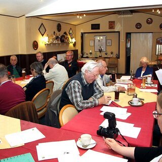 Menschen die an Tischen sitzen und auf Zetteln lesen