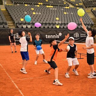 Kinder beim Tennistraining üben Koordination mit Luftballons